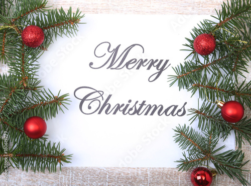 Text merry christmas on paper with fur-tree  branches  colored glass balls   decoration and cones on a wooden background
