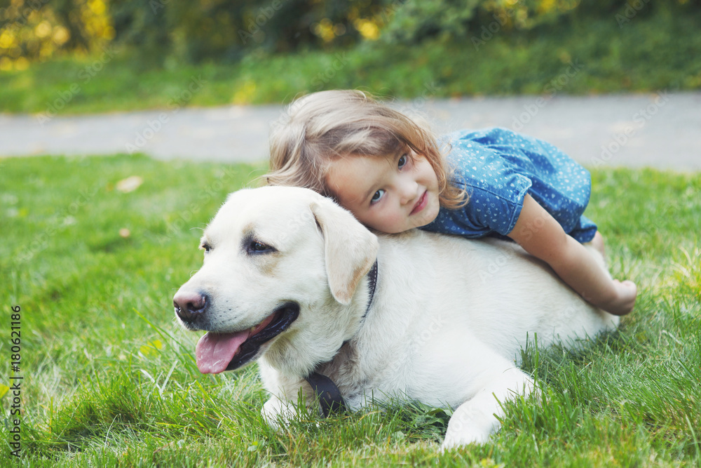 Little girl sitting on the grass with labrador retriever in the summer park Little girl sitting on the grass with labrador retriever in the summer park
