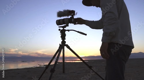 Photo Lake Sunset / Person operating a camera mounted on a tripod in front of a lake during sunset. photo