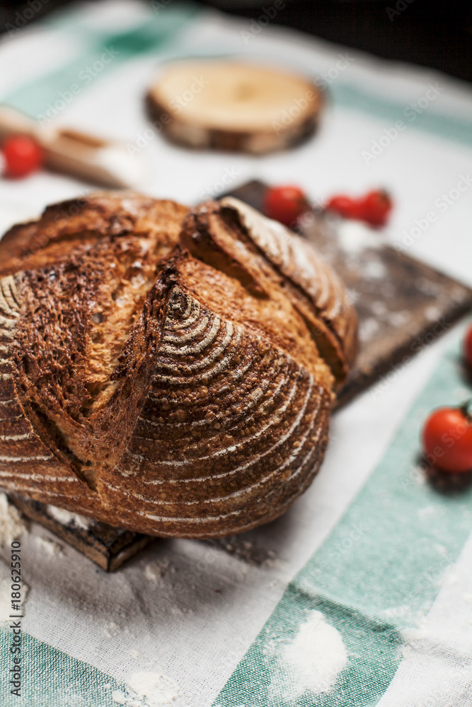 freshly baked bread, flour and tomatoes on a wooden board on a kitchen towel on a table freshly baked bread, flour and tomatoes on a wooden board on a kitchen towel on a table