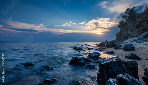 Beautiful sunset near the sea with waves over the rocks and sun between the clouds