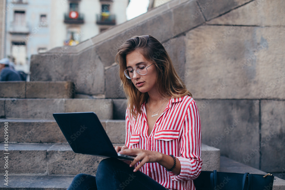 Pretty young woman or student girl sits or rests on steps of office building or university, works on laptop, browses internet for online shopping or business projects, concept freelance or startup Pretty young woman or student girl sits or rests on steps of office building or university, works on laptop, browses internet for online shopping or business projects, concept freelance or startup