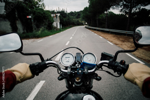 POV from drivers point of view of motorcycle handlebar with speedometer and rear view windows, driving on quiet empty mountain road, driver wears leather gloves and steers confidently