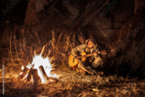 Armed rebel resting by the fire and playing the guitar