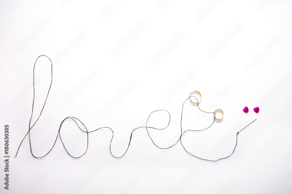 word love written with black thread and the needle inserted two gold wedding bands, there are two pink hearts and white background word love written with black thread and the needle inserted two gold wedding bands, there are two pink hearts and white background