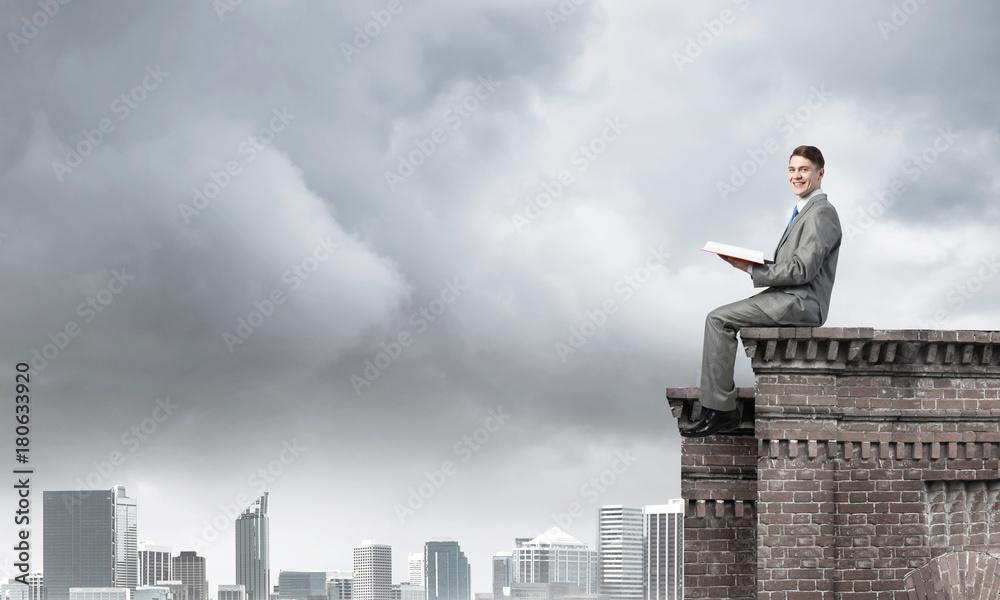 Man on roof edge reading book and cityscape at background Man on roof edge reading book and cityscape at background
