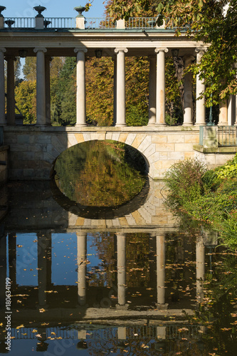 Reflection in water of the stone footbridge with ionic columns in Warsaw Royal Baths Park on a sunny autumnal day