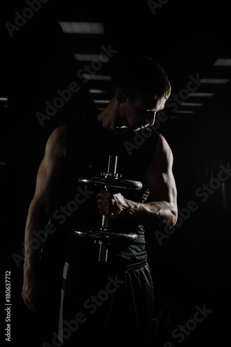 Strong Athletic Man Fitness Model Torso showing six pack abs. isolated on black background with copyspace Closeup of a handsome power athletic man bodybuilder doing exercises with dumbbell.