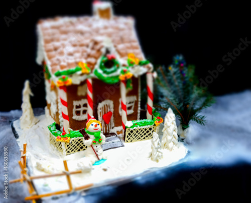 Big gingerbread house, a sprig of Christmas tree and a sugar mastic snowman on dark background © kolotype