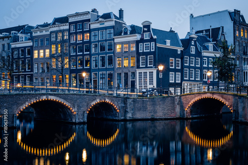 Old historic houses, canal, bridge and a yellow light trail during twilight blue hour, Amsterdam, Netherlands