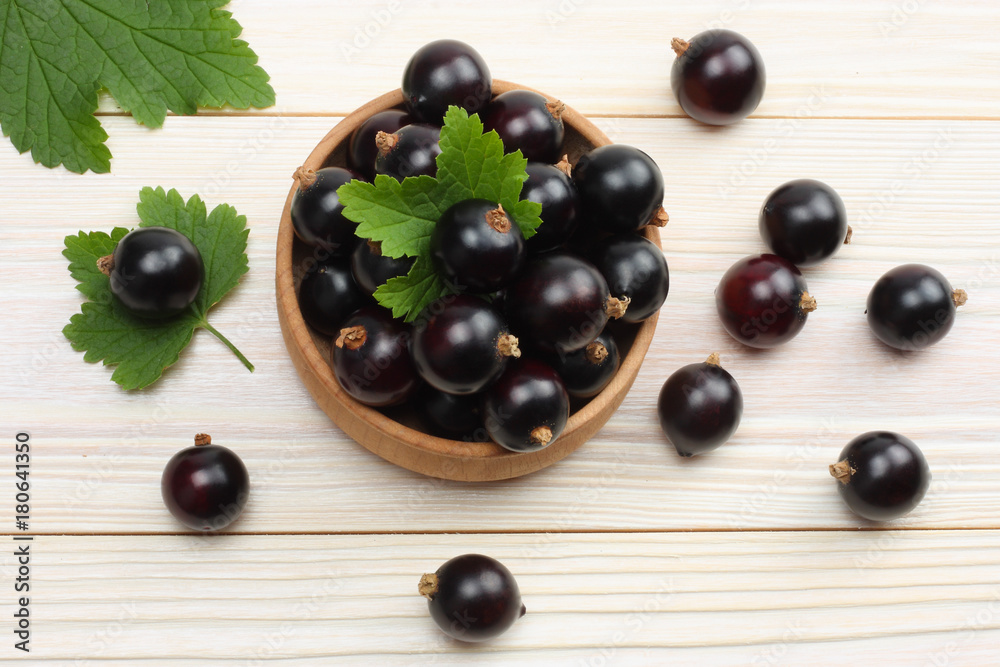 black currant in wooden bowl with green leaf on white wooden background. top view with copy space black currant in wooden bowl with green leaf on white wooden background. top view with copy space