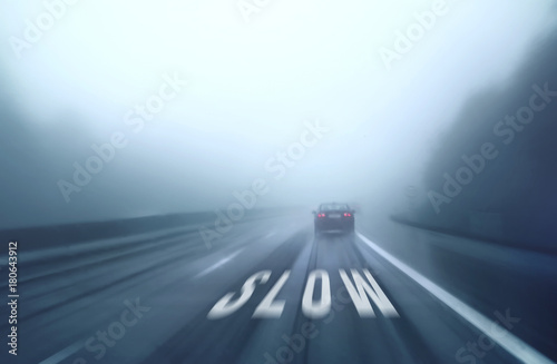 Car drive along a slippery highway with slow warning mark on the asphalt ground. Rainy and foggy conditions with poor visibility on the road. Personal perspective used. photo