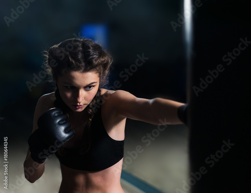 Beautiful young fighter boxer fit girl wearing boxing gloves in training, focused on heavy punching bag in gym. She is in good shape. Woman power © Igor Kardasov