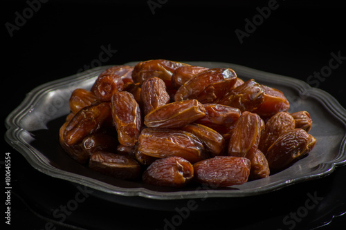 Sweet dessert dried date in old tin bowl, low key, dark theme, on black background with reflection