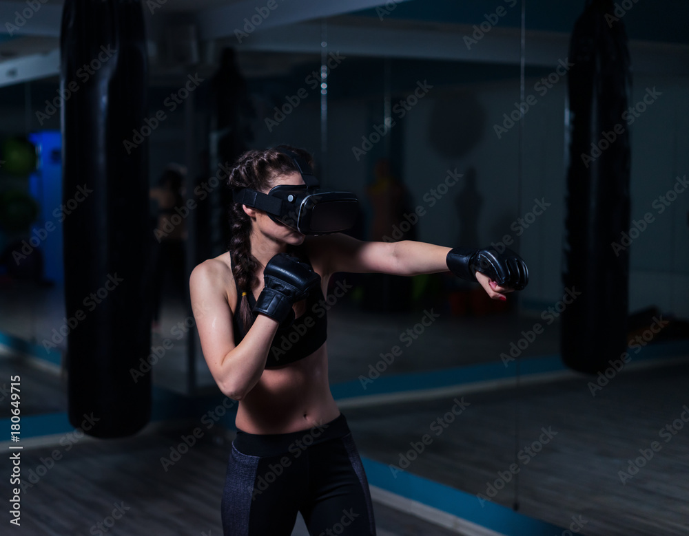 Young fighter boxer fit girl in VR glasses wearing boxing gloves in training. Boxing game in virtual reality 360 degrees. Futuristic gaming