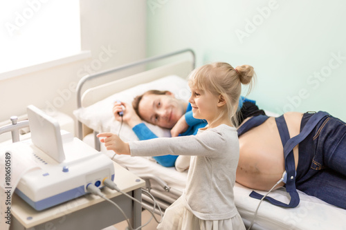Pregnant woman with daughter smiling and looking to the display during pregnancy examination in hospital while waiting for newborn