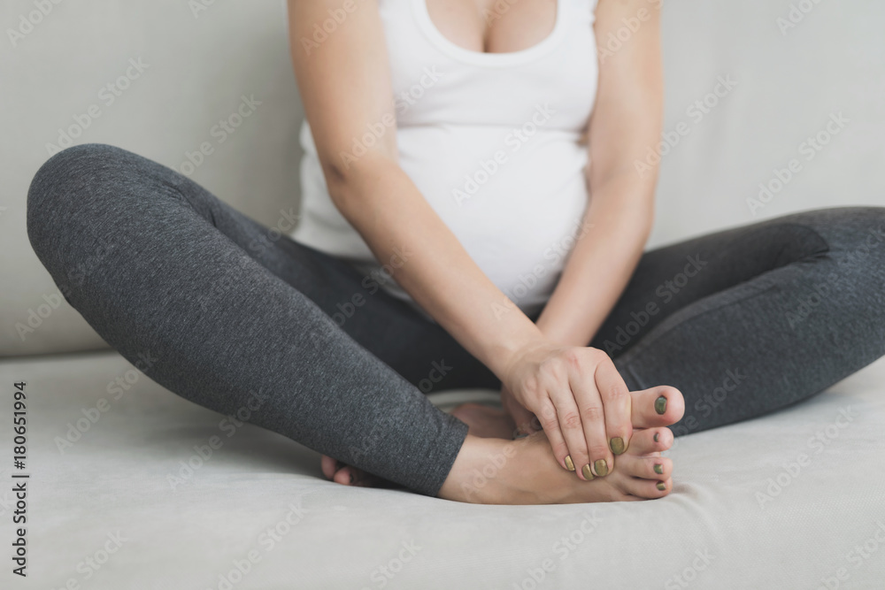 A pregnant woman sits at home on a light sofa. Her legs hurt