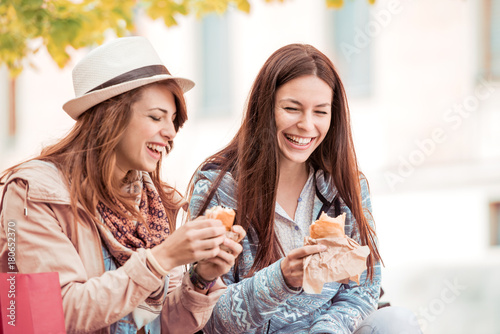 Two beautiful girls eating sandwiches after shopping.