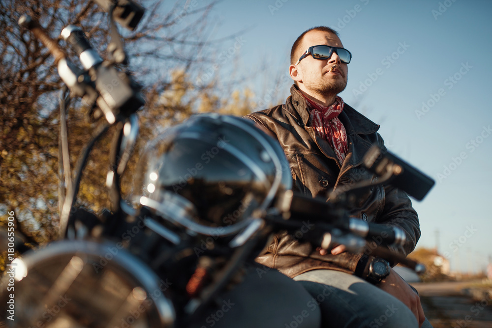 young man motorcyclist smokes a cigarette while sitting on a motorcycle