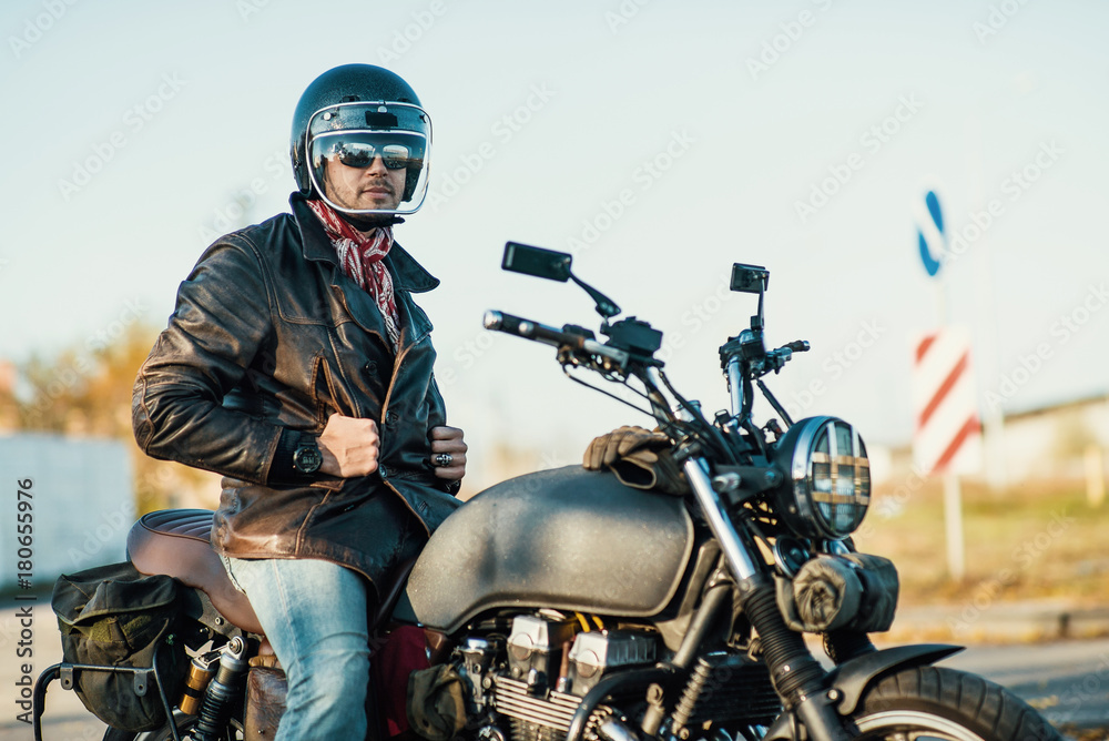 Obraz premium Motorcyclist sits on an old cafe-racer motorcycle, autumn background
