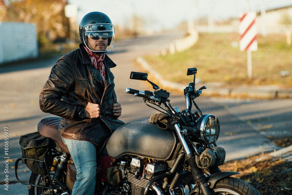 Motorcyclist sits on an old cafe-racer motorcycle, autumn background Motorcyclist sits on an old cafe-racer motorcycle, autumn background