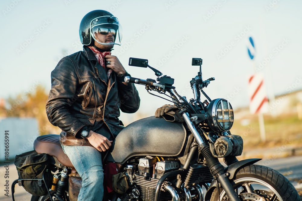 Motorcyclist sits on an old cafe-racer motorcycle, autumn background Motorcyclist sits on an old cafe-racer motorcycle, autumn background