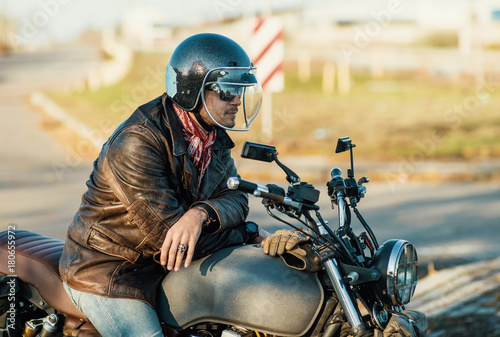 Motorcyclist sits on an old cafe-racer motorcycle, autumn background