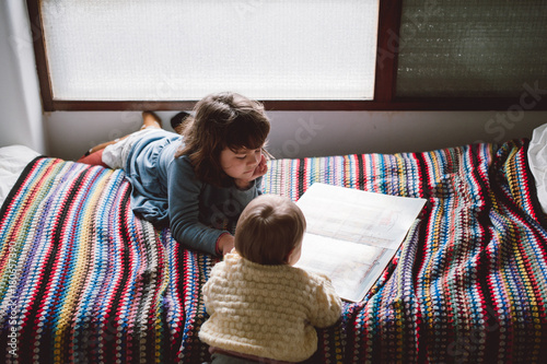 little girl and baby with a book on a bed