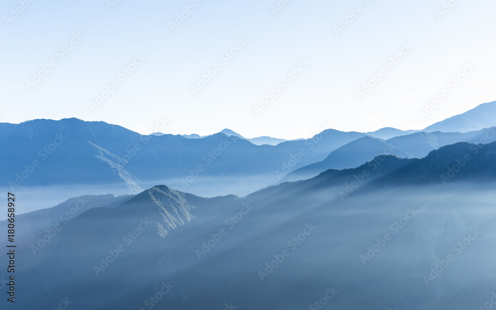 Hazy blue mountains of Zhushan inside Alishan Recreation Area in Taiwan covered by fog during sunrise in morning with bright winter sky.