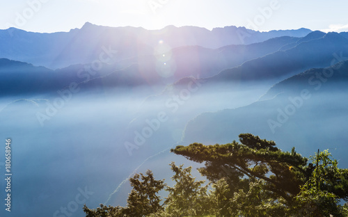 Hazy blue mountains of Zhushan inside Alishan Recreation Area in Taiwan covered by fog during sunrise in morning with bright winter sky. photo