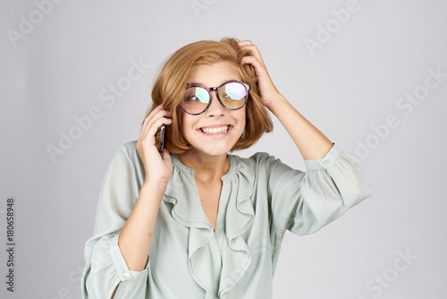 cheerful girl in big glasses with a phone on a light background