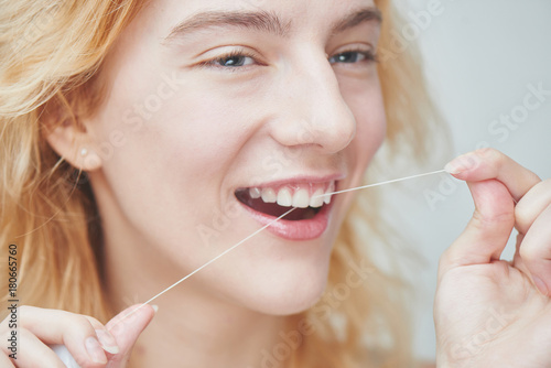 Young girl brushing her teeth with dental floss  close up on white background