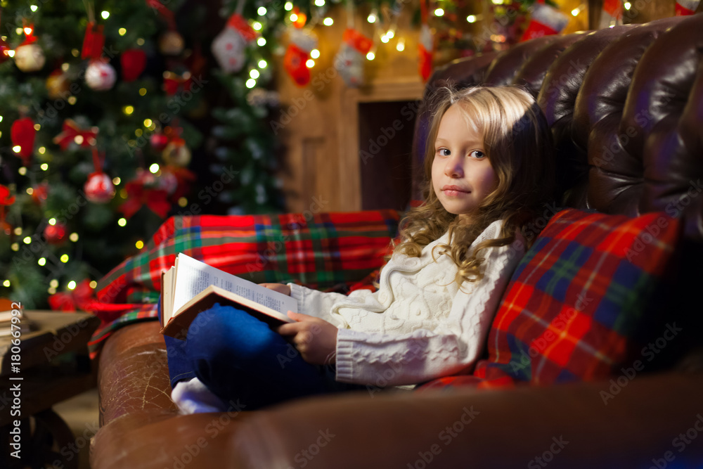 Happy little girl reading a story book by on the couch in a cozy Happy little girl reading a story book by on the couch in a cozy