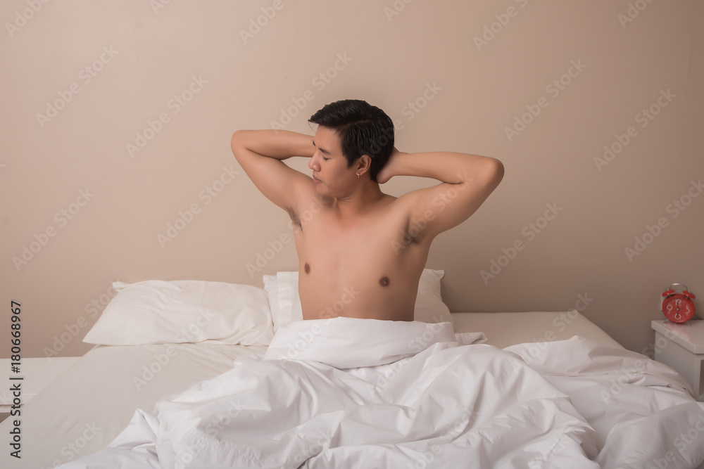 Handsome man smiling while stretching in his bed at home Handsome man smiling while stretching in his bed at home