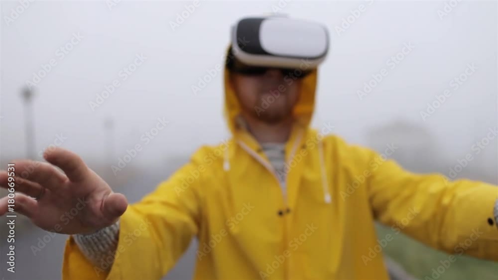 man in virtual reality glasses and a yellow raincoat by foggy street man in virtual reality glasses and a yellow raincoat by foggy street