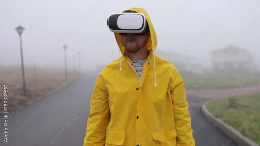 man in virtual reality glasses and a yellow raincoat by foggy street man in virtual reality glasses and a yellow raincoat by foggy street