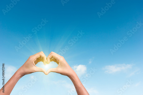 hands making a heart shape in the blue sky with sunlight