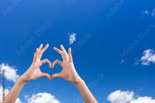 two hands making a heart shape in the blue sky