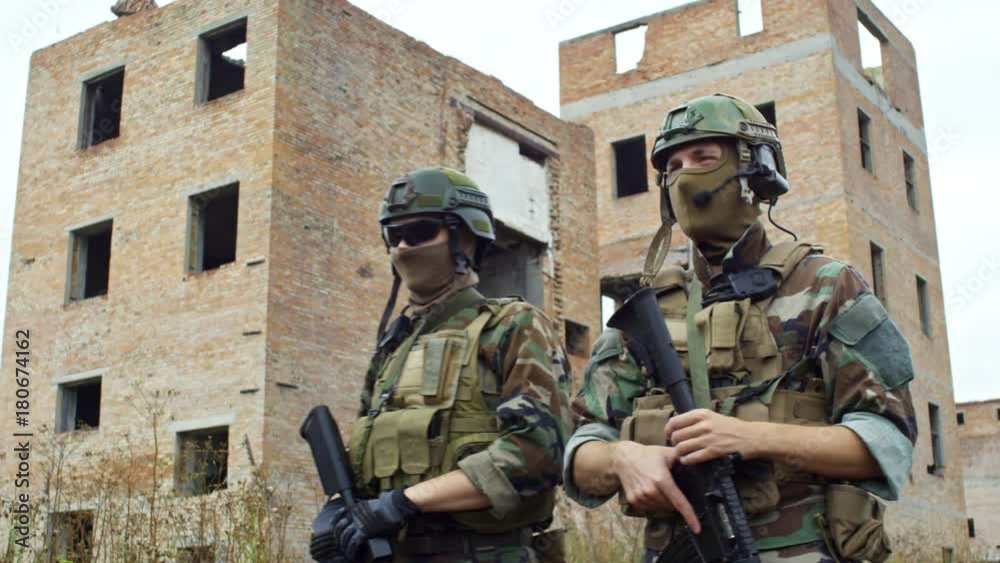 SLOWMO of special forces troop walking with shotguns through abandoned area with derelict buildings