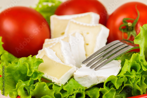 Tomatoes and cheese slices lie on a sheet of fresh salad in a red plate.