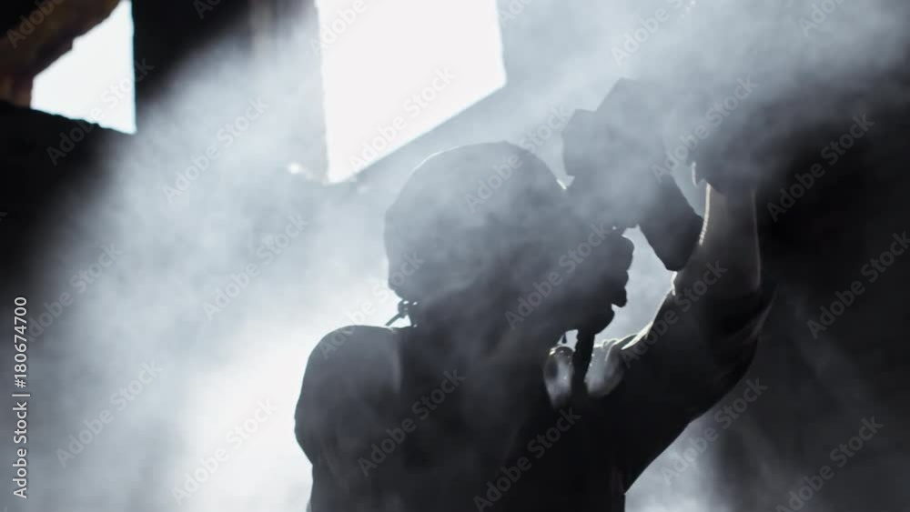 Low angled shot of soldier aiming shotgun and walking through smoke in abandoned building