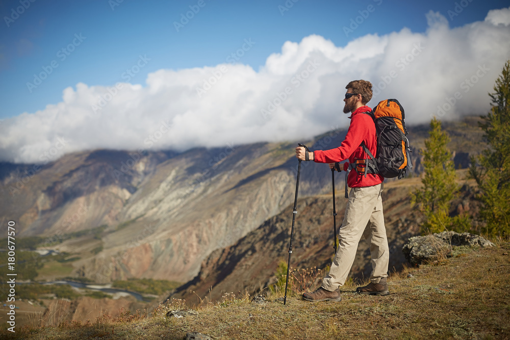 Handsome young bearded male hiker sitting on the edge of a canyon looking away