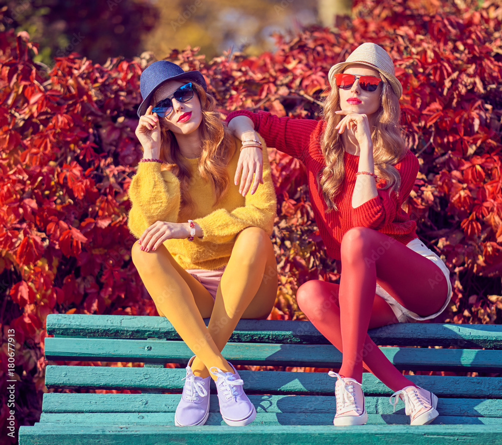 Fall Fashion. Two Girls Sitting on Bench in Colorful Park. Young Woman  Enjoy Nature, Urban Outdoor. Friends Model in Stylish Trendy fashion Autumn  Outfit, Glamour Sunglasses foto de Stock | Adobe Stock
