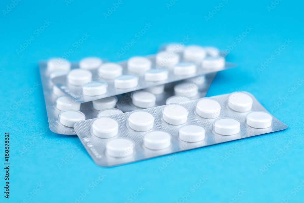 Packs of white pills packed in blisters with copy space on blue background. Focus on foreground, soft bokeh