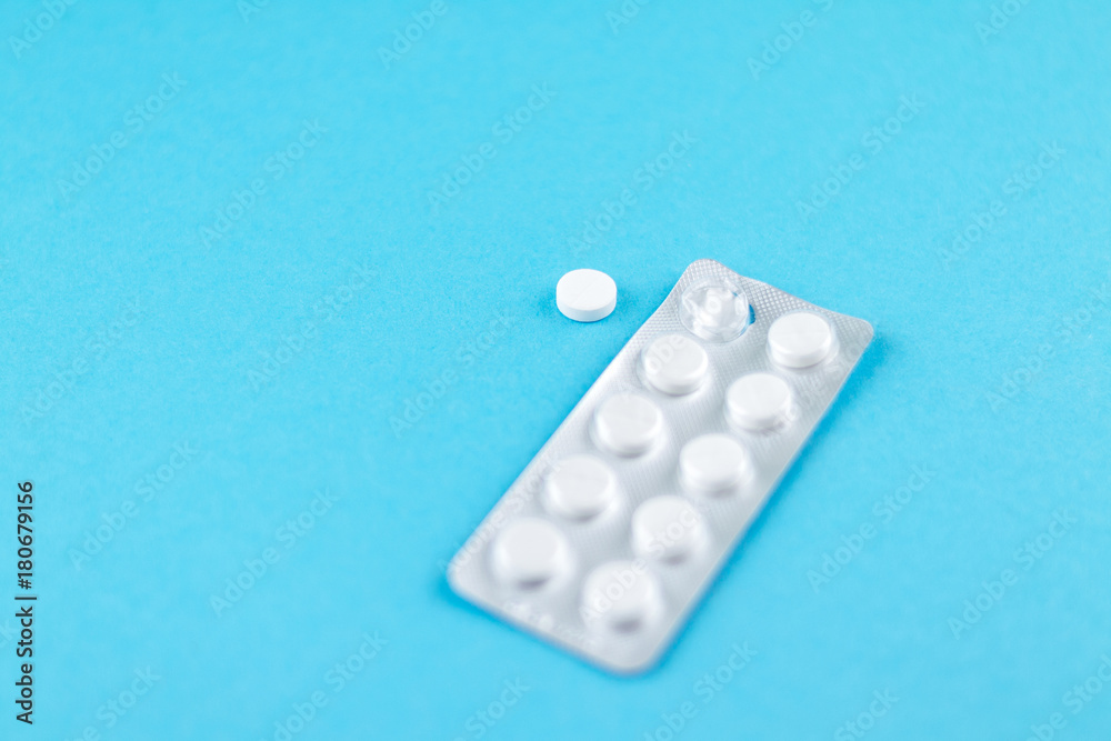 Packs of white pills packed in blisters with copy space on blue background. Focus on foreground, soft bokeh