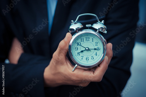 Businessman holding the retro clock in front of the white car