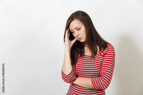 Pretty European young worried and pensive brown-haired woman with healthy clean skin, dressed in casual red and grey clothes lost in thought and conjectures, on a white background. Emotions concept.