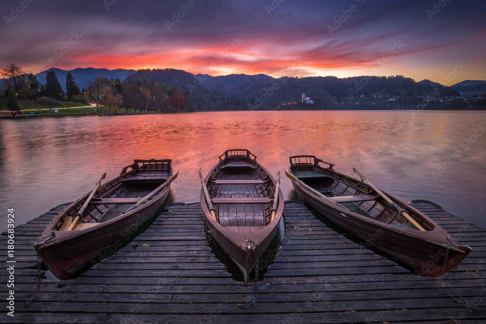 Bled, Slovenia - Traditional boats at Lake Bled with beautiful dramatic sunset and the Assumption of Mary Pilgrimage Church and mountains at background at sunset 
