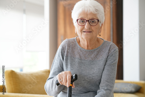 Portrait of elderly woman sitting in sofa, holding cane