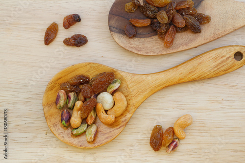 Nuts and raisins mix in wooden spoon / spatula on wooden table. Nuts include pistachio, macadamia and cashew. Copy space.